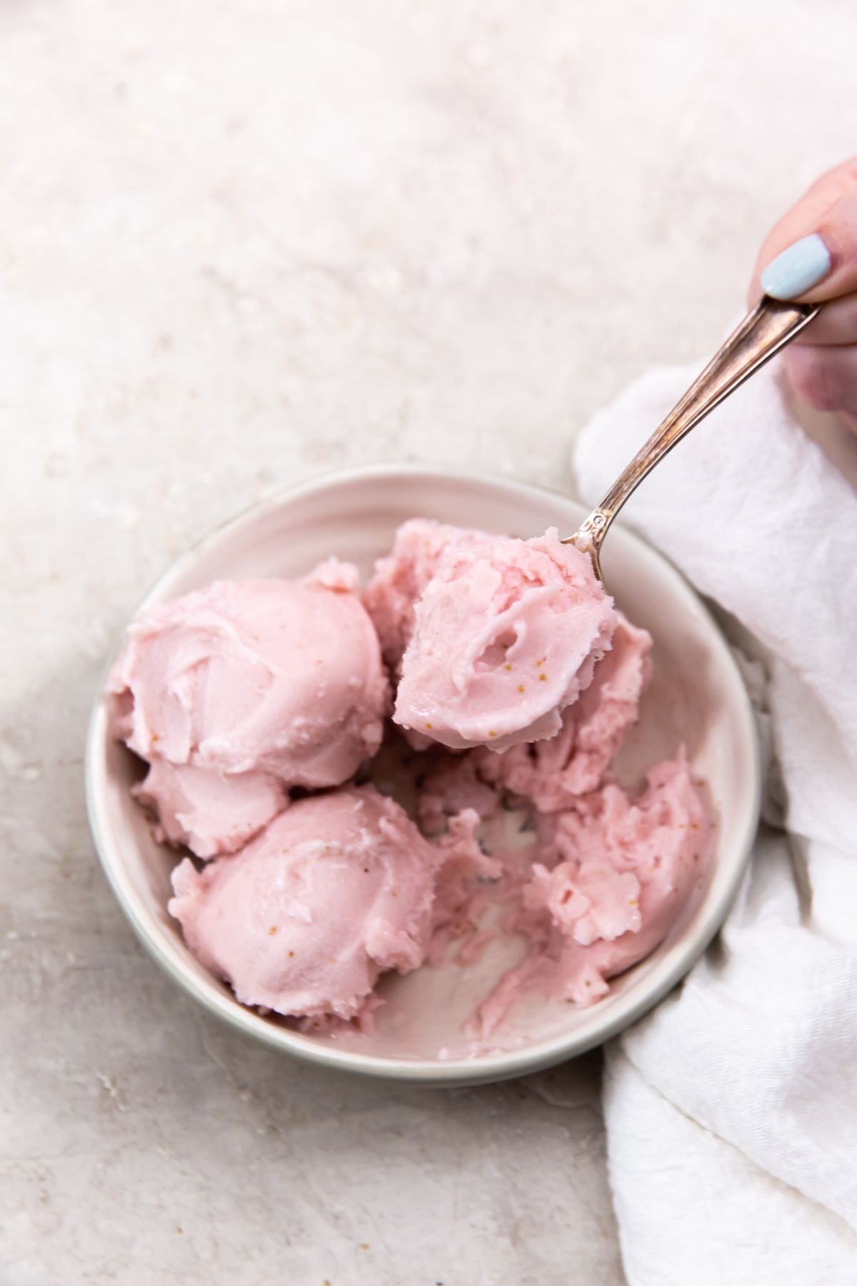 keto strawberry ice cream in a bowl with a hand picking up the spoon