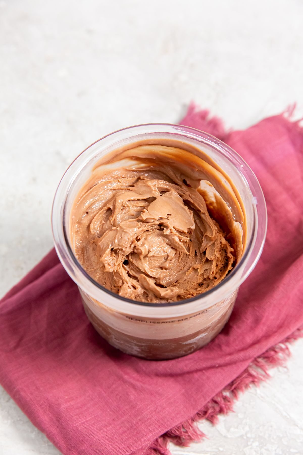 Chocolate protein ice cream in clear container on pink towel