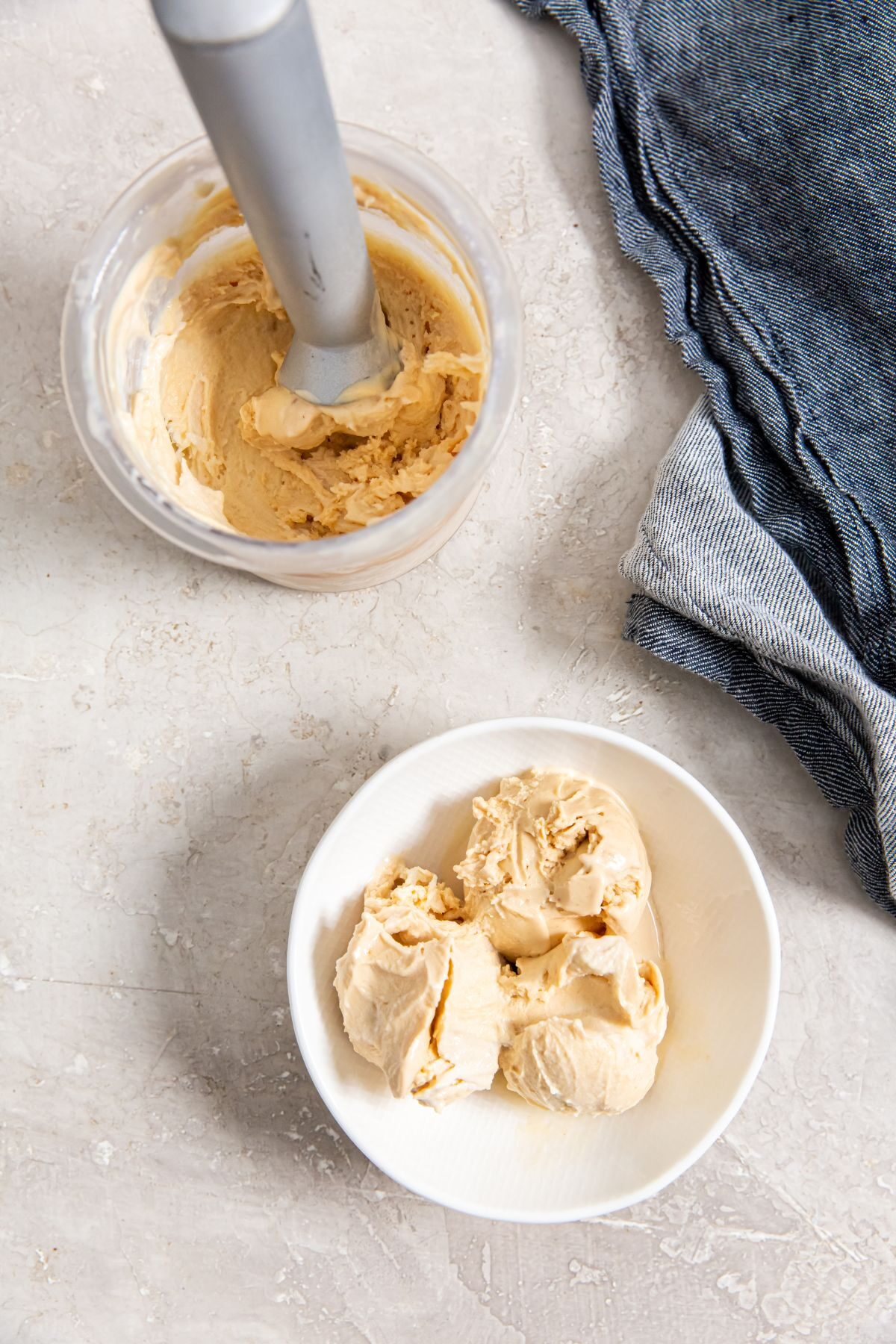 Peanut butter ice cream in a pint jar with scoop and 3 scoops of ice cream in white bowl next to a blue napkin