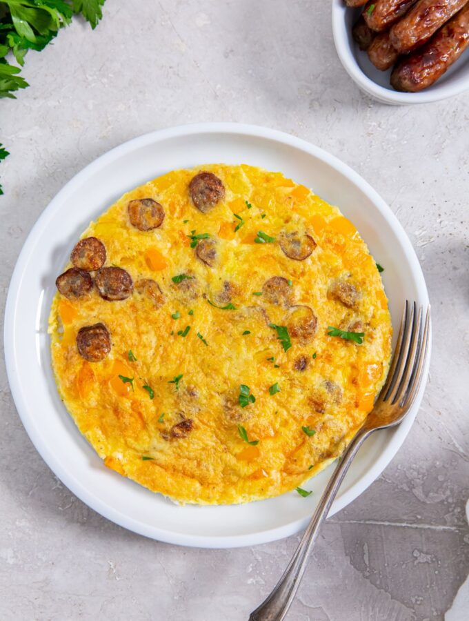 air fryer omelet on a white plate with a fork with sausage on the side
