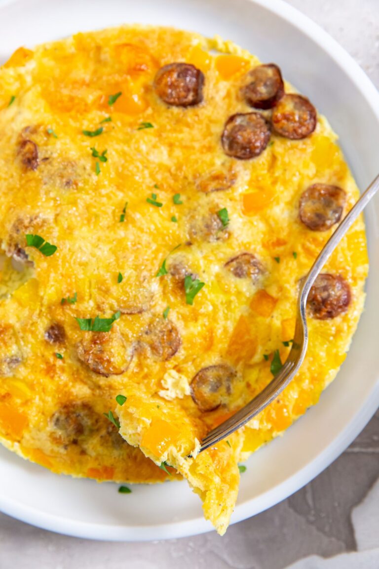 Air Fryer Omlette with bell peppers, parsley, cheese, and sausage on a white plate with a fork.