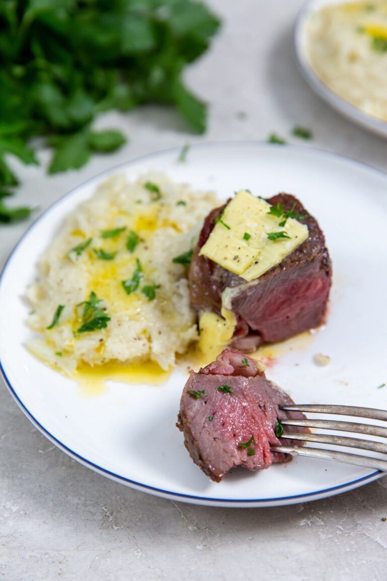 Air Fryer Bacon Wrapped Chuck Tender Filet on a what plate with mashed cauliflower, butter, parsley, pepper, and salt.