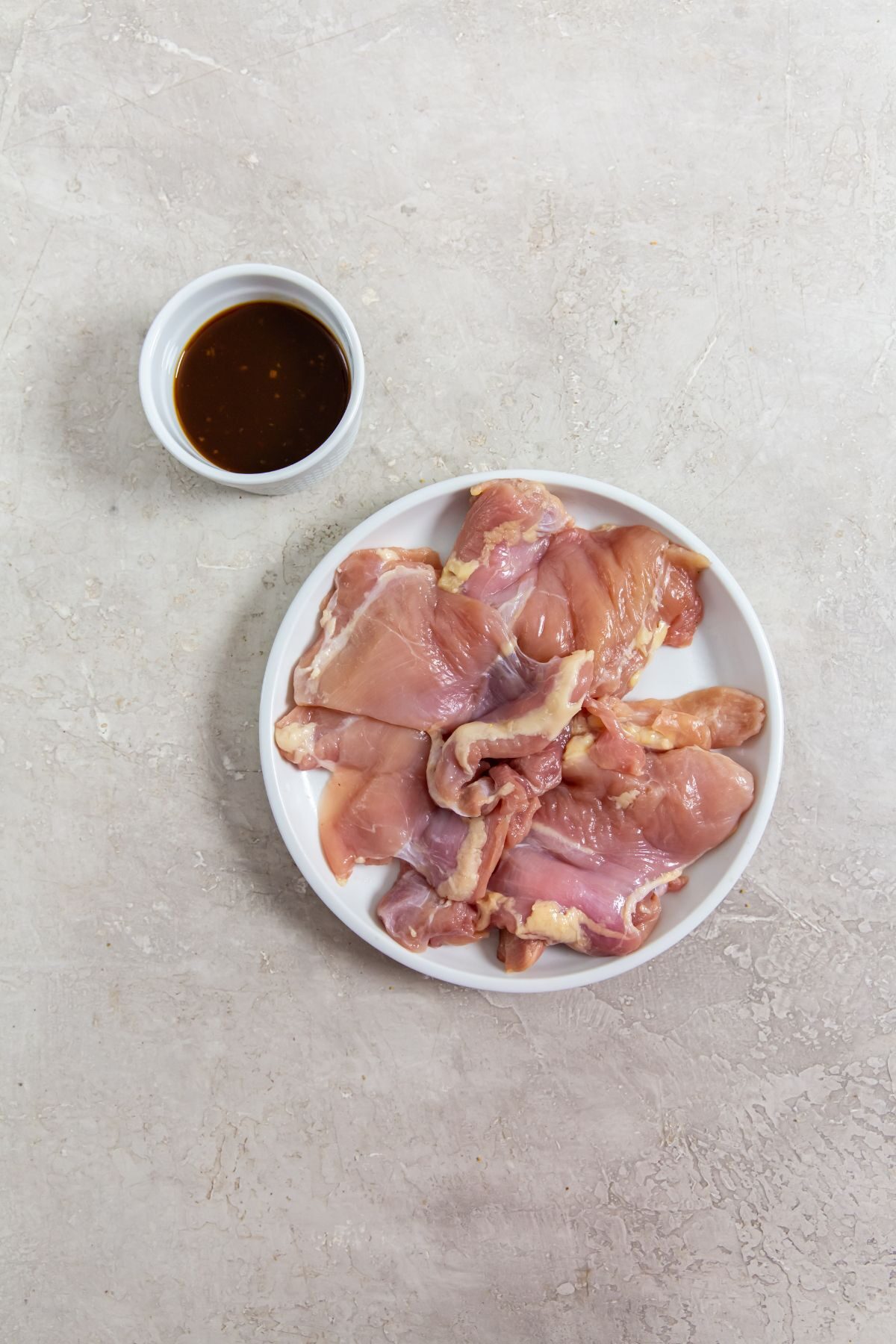 ingredients of raw chicken thighs and paleo teriyaki sauce on a white plate