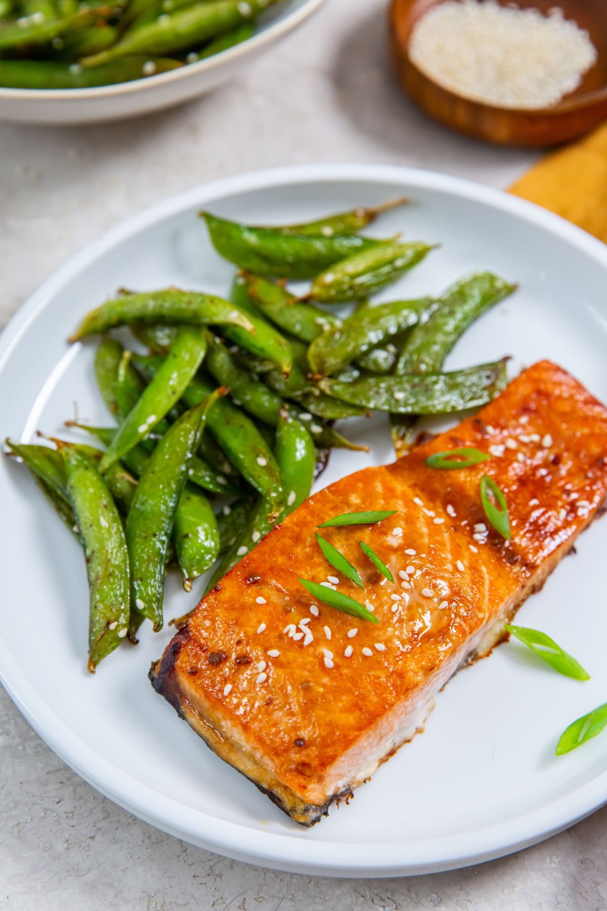 Air Fryer frozen salmon with teriyaki sauce on a white plate with a side of snap peas