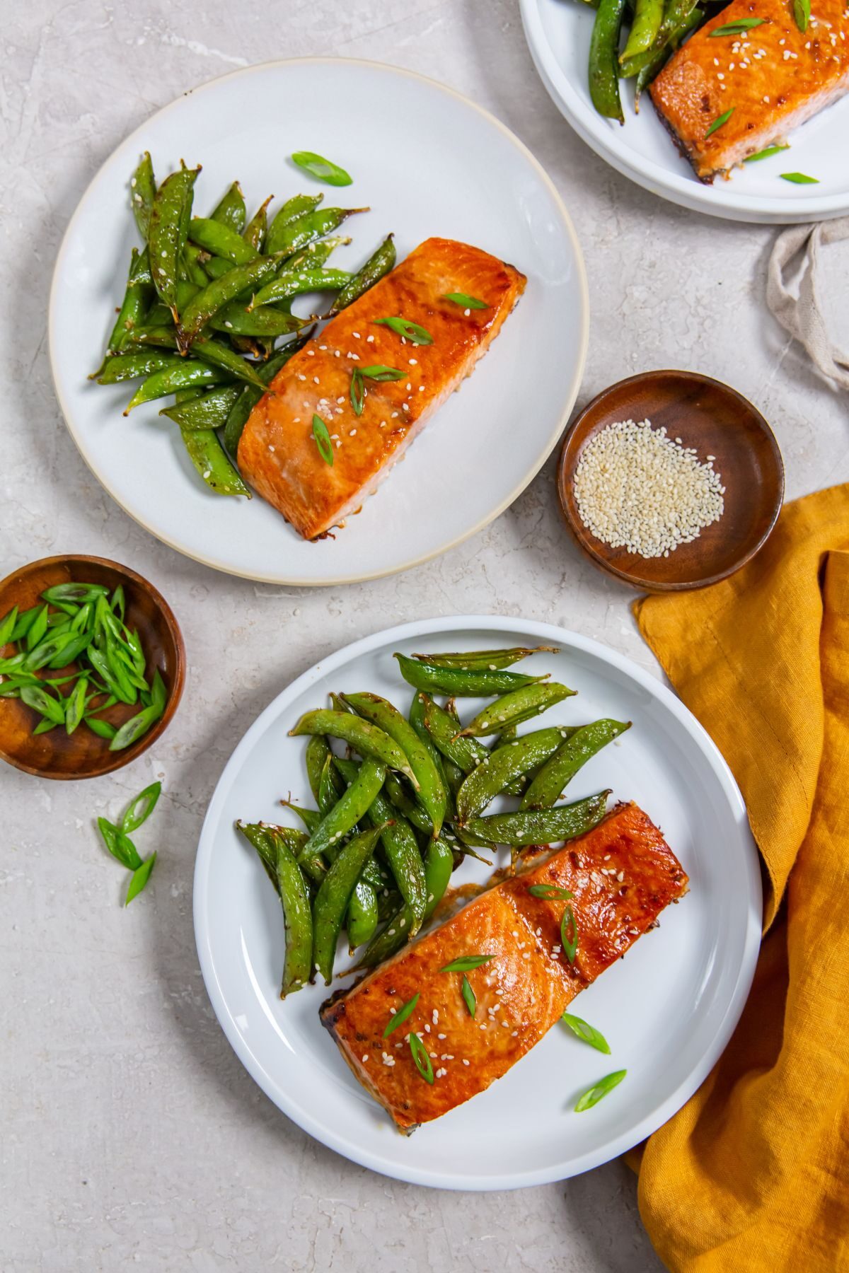 Two plate of Air Fryer frozen salmon with teriyaki sauce on a white plate with a side of snap peas