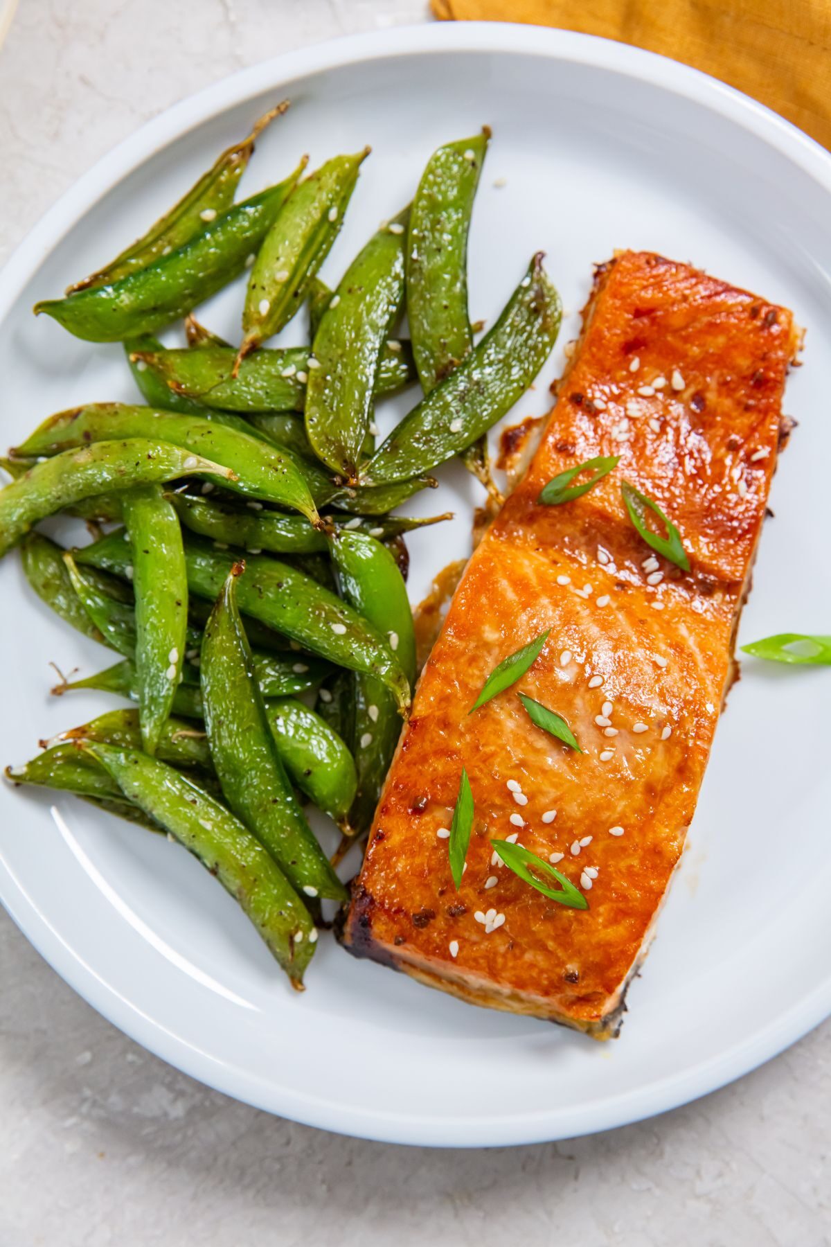 Air Fryer frozen salmon with teriyaki sauce on a white plate with a side of snap peas