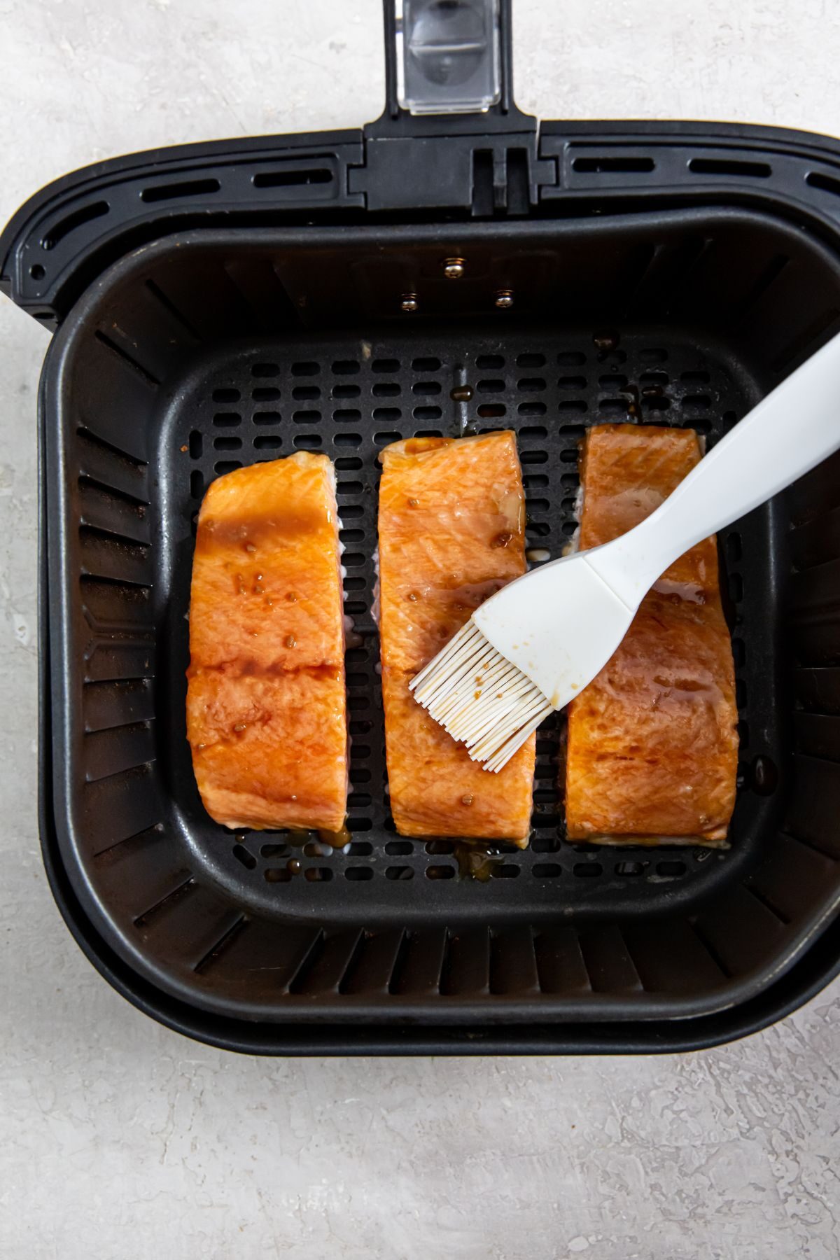 Air Fryer frozen salmon with teriyaki sauce in the air fryer basket with a white brush
