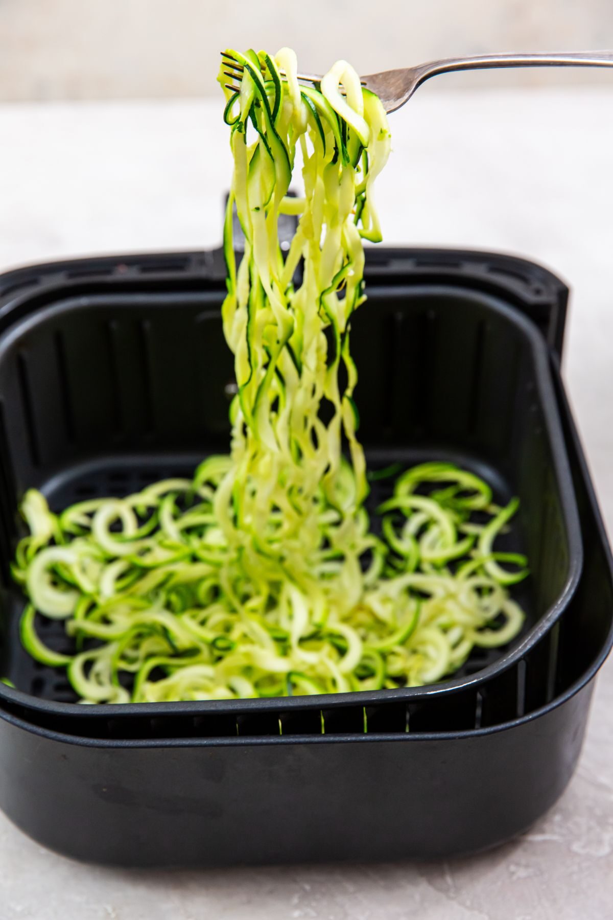 Zoodles in the air fryer basket with a fork holding it up