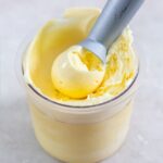 ninja creami eggnog ice cream in a clear pint container with an ice cream scoop