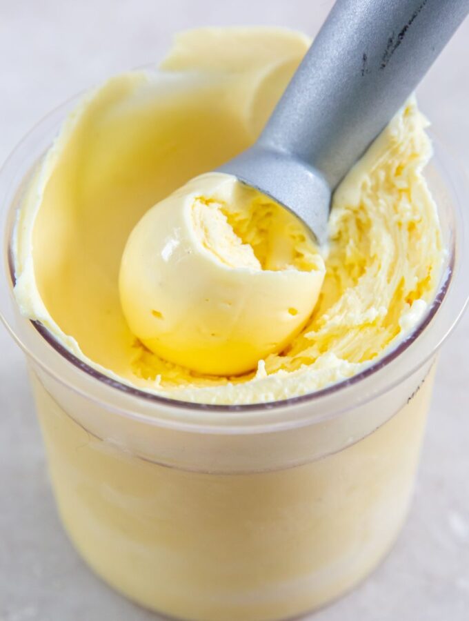 ninja creami eggnog ice cream in a clear pint container with an ice cream scoop