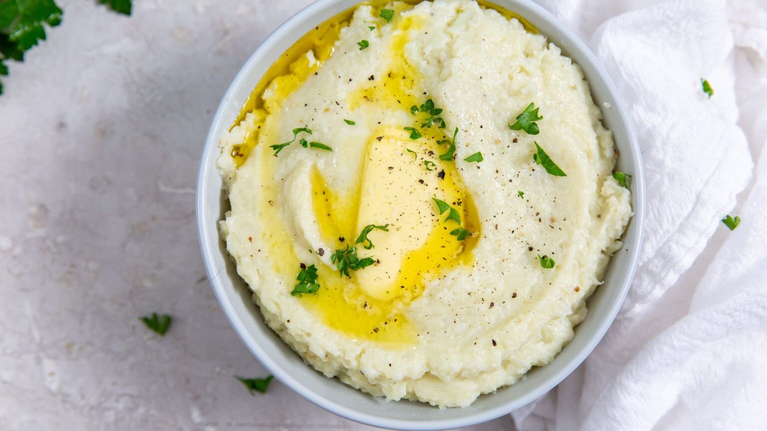 Instant Pot Cheesy Mashed Cauliflower in a white bowl with butter, salt, pepper, and parsley.