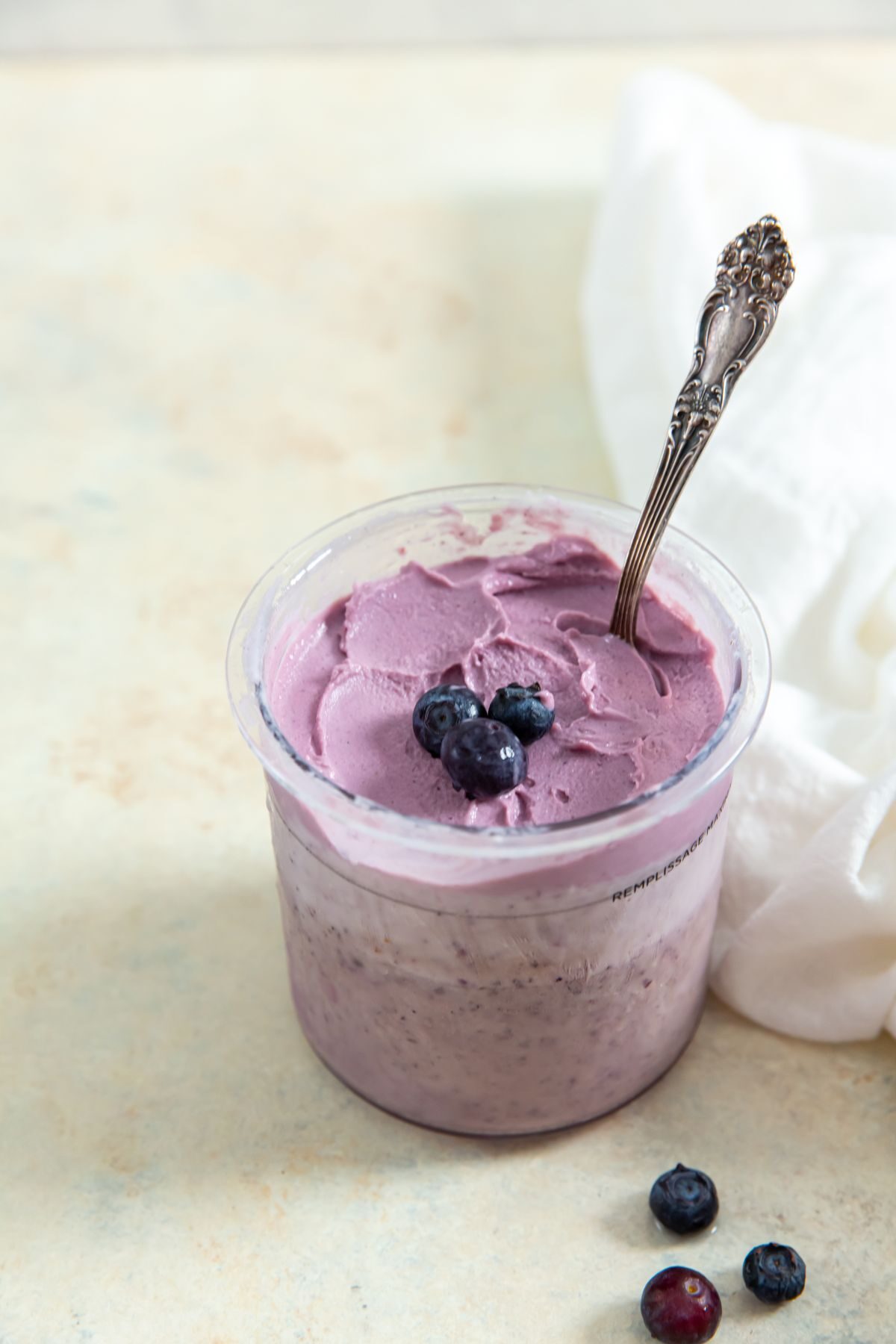ninja creami low carb blueberry frozen yogurt in a pint with a spoon in it with blueberries on top and a white napkin on the side