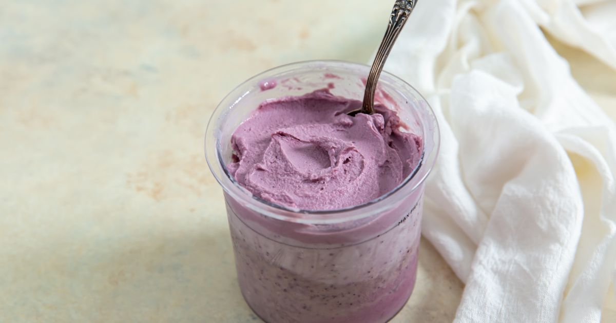 ninja creami low carb blueberry frozen yogurt in a pint with a spoon in it with a white napkin on the side