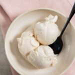 Snickerdoodle ice cream in a white bowl with a spoon and pink napkin on the side.