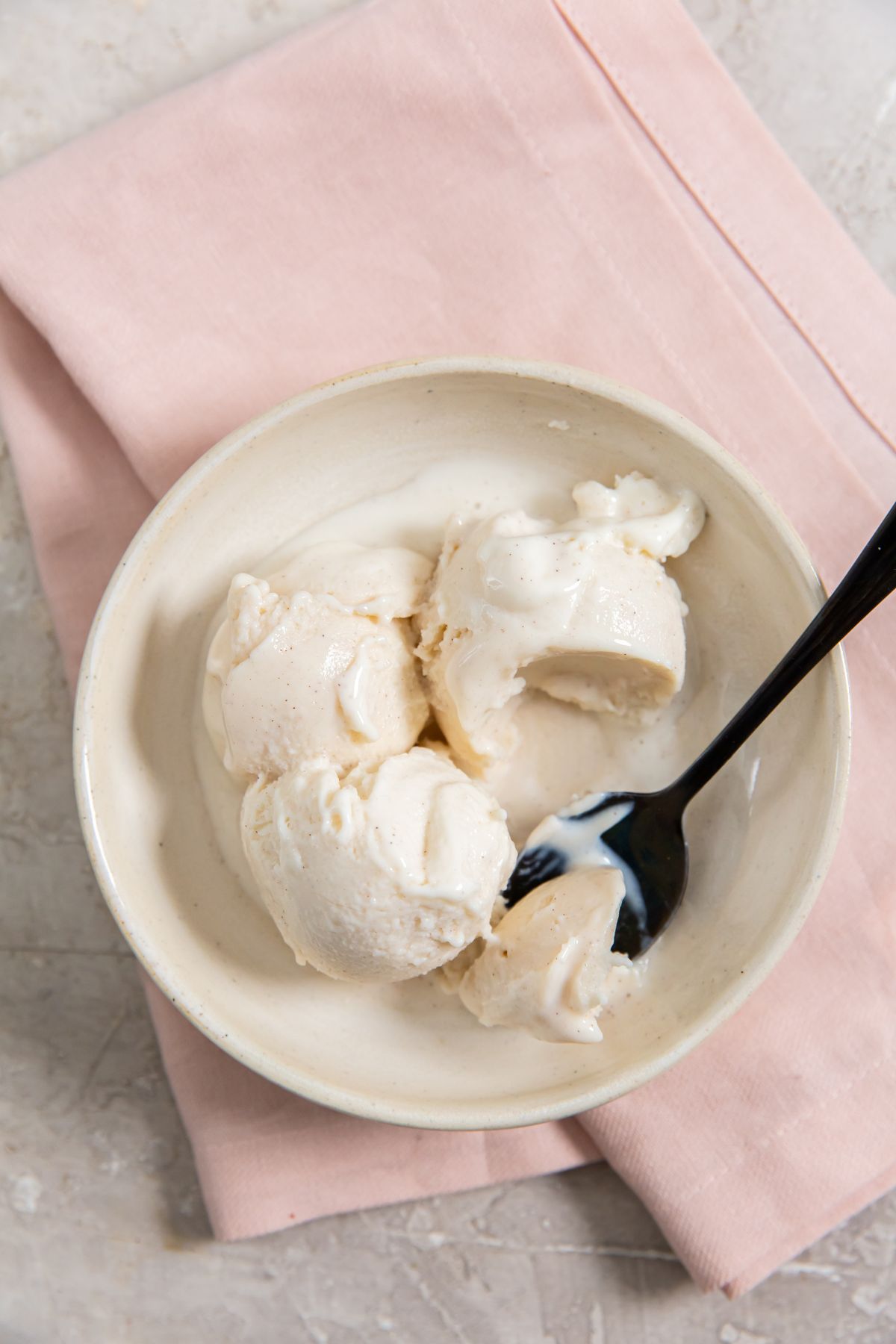 Snickerdoodle ice cream in a white bowl with a spoon and pink napkin on the side.