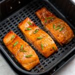 cooked frozen salmon filets in an air fryer basket topped with scallions and sesame seeds