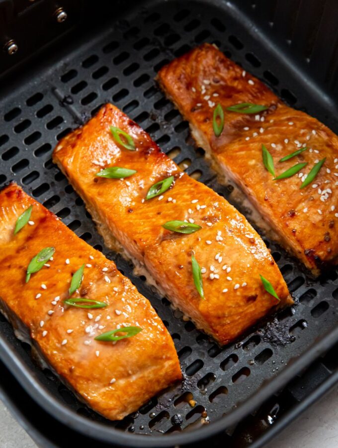 cooked frozen salmon filets in an air fryer basket topped with scallions and sesame seeds