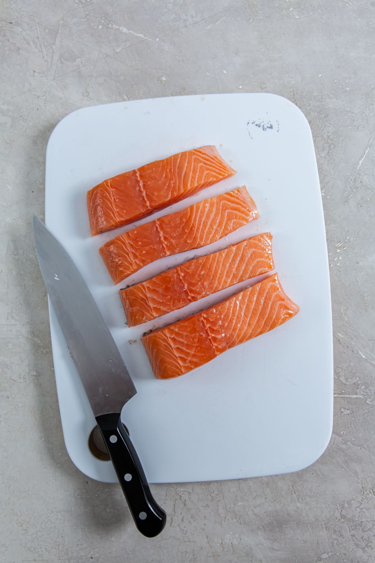 raw salmon on a cutting board sliced into four pieces with a knife on the side