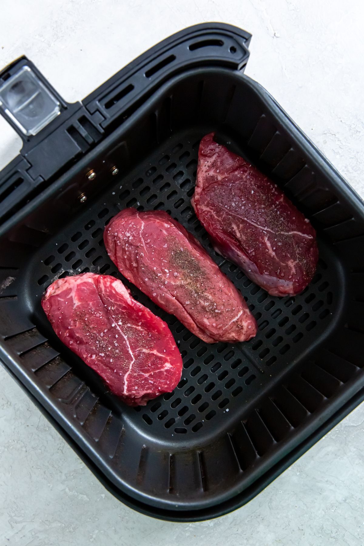 Three raw petite sirloin steaks in an air fryer.