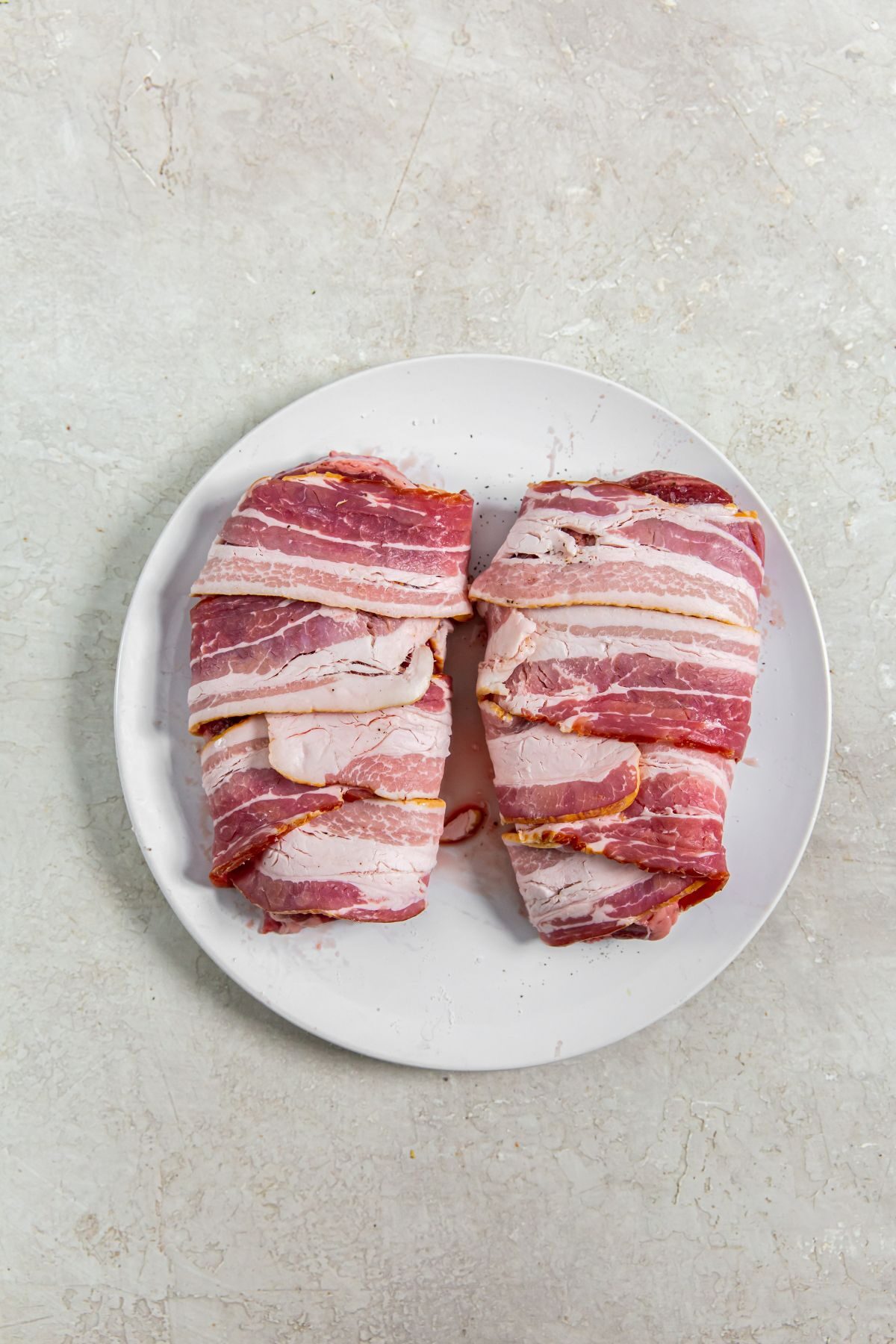 raw bacon wrapped ribeye steak on a white plate