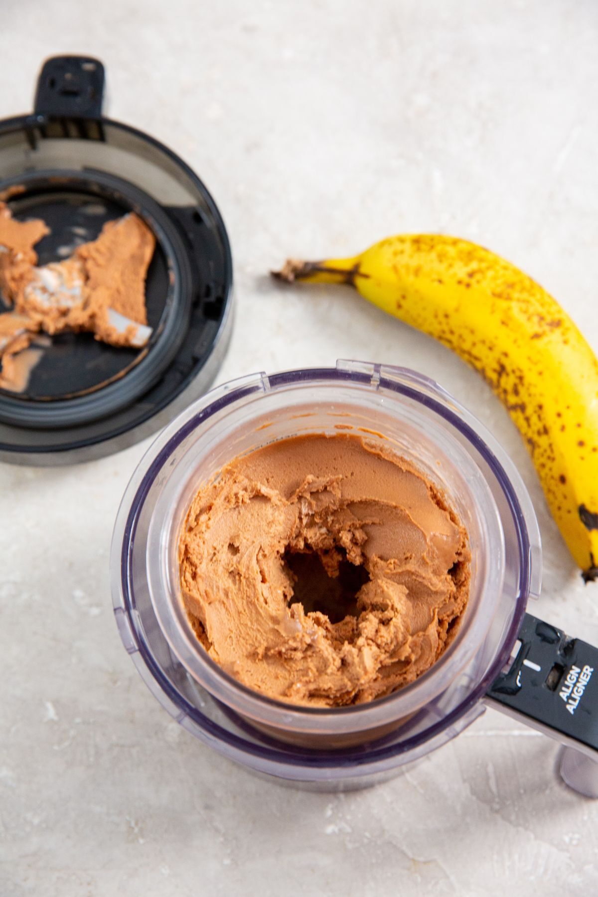 Chocolate Banana Protein Ice Cream in the ninja creami pint holder and bananas in the background