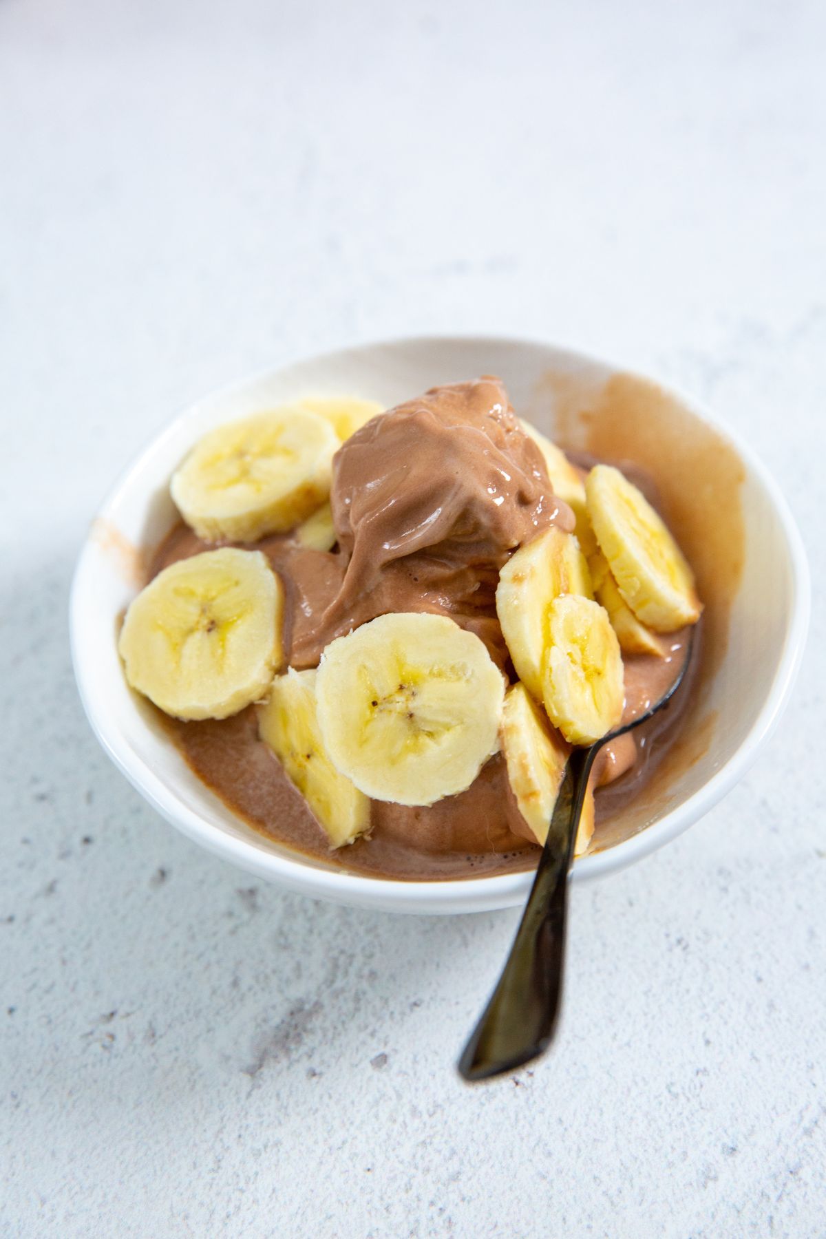 Chocolate Banana Protein Ice Cream in a white bowl with banana slices on top and a spoon in it