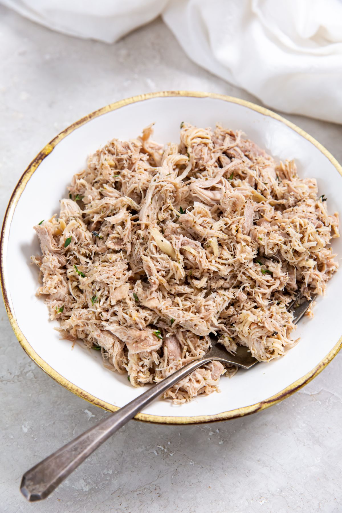 Instant Pot shredded frozen chicken thighs on a white plate with a fork and a white napkin on the side