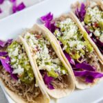 Low Carb Shredded Chicken Tacos on a white plate with cabbage, guacamole and cheese on top and a sliced lime on the side