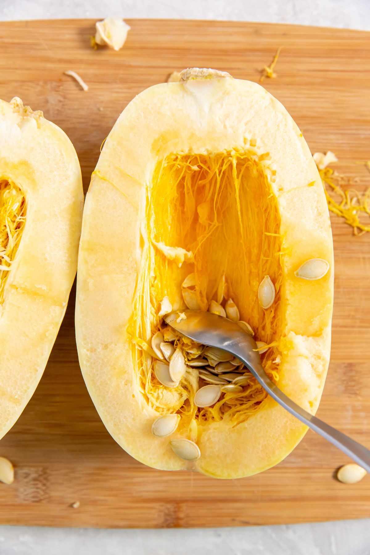 Spaghetti Squash on a cutting board with a spoon scooping out the seeds
