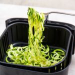 air fryer zoodles being pulled out of the basket with a fork.