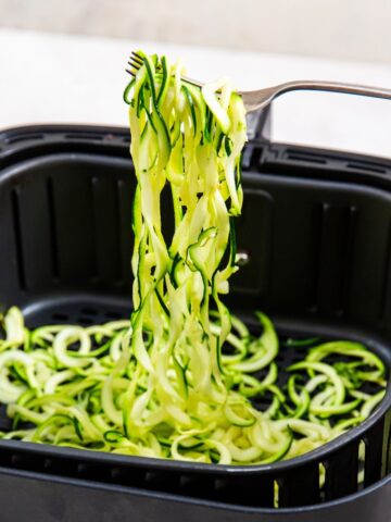 air fryer zoodles being pulled out of the basket with a fork.