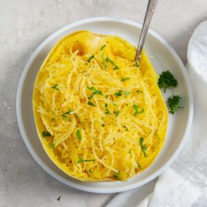 cooked whole spaghetti squash cut in half on a white plate topped with parsley