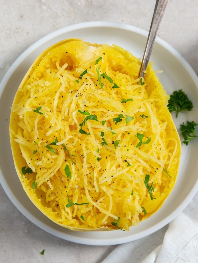 cooked whole spaghetti squash cut in half on a white plate topped with parsley