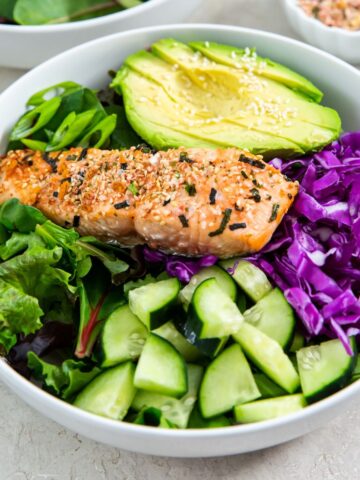 sesame salmon bowl with avocado, red cabbage, cucumber and spring mix topped with sesame dressing.