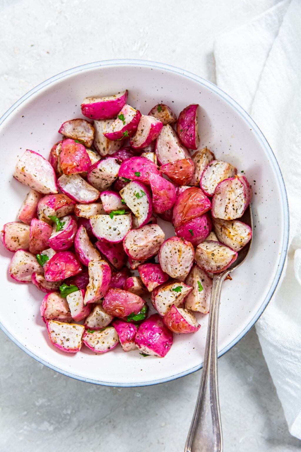 Air Fryer Radishes with parsley, salt, and pepper in a white bowl with a spoon.