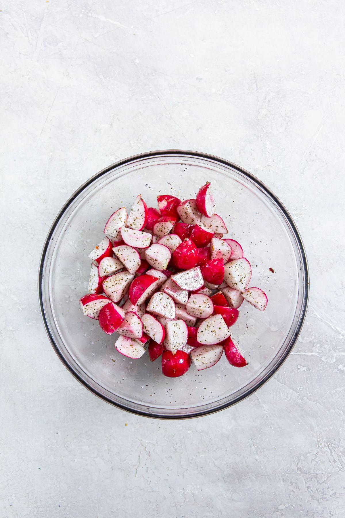 cut radishes in a clear bowl with seasonings on top