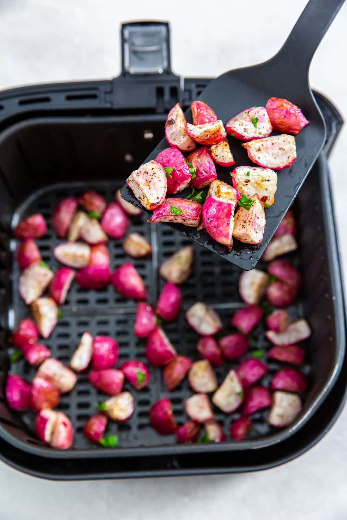 Air fryer radishes in the air fryer basket with a spatula lifting up some
