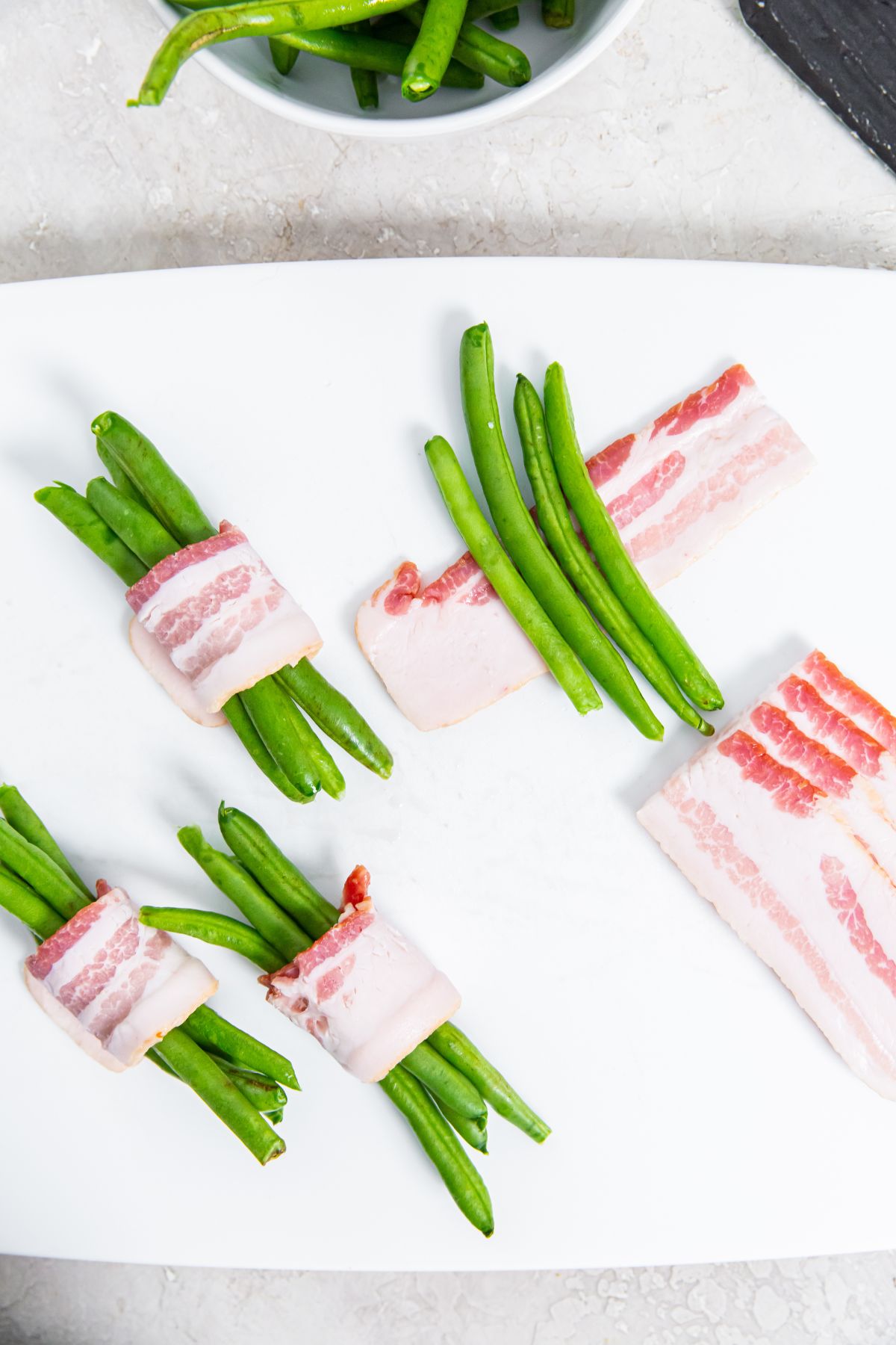 white cutting board with green beans being wrapped in bacon