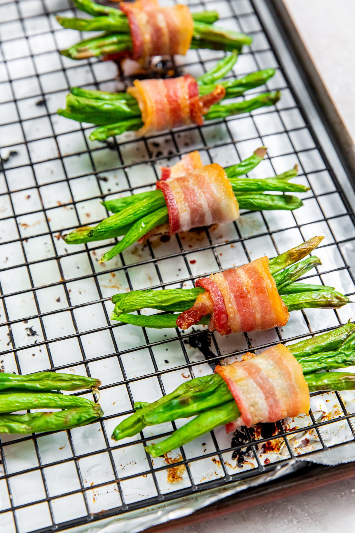 Bacon Wrapped Green Beans on a cooling rack on top of a foil lined baking pan.