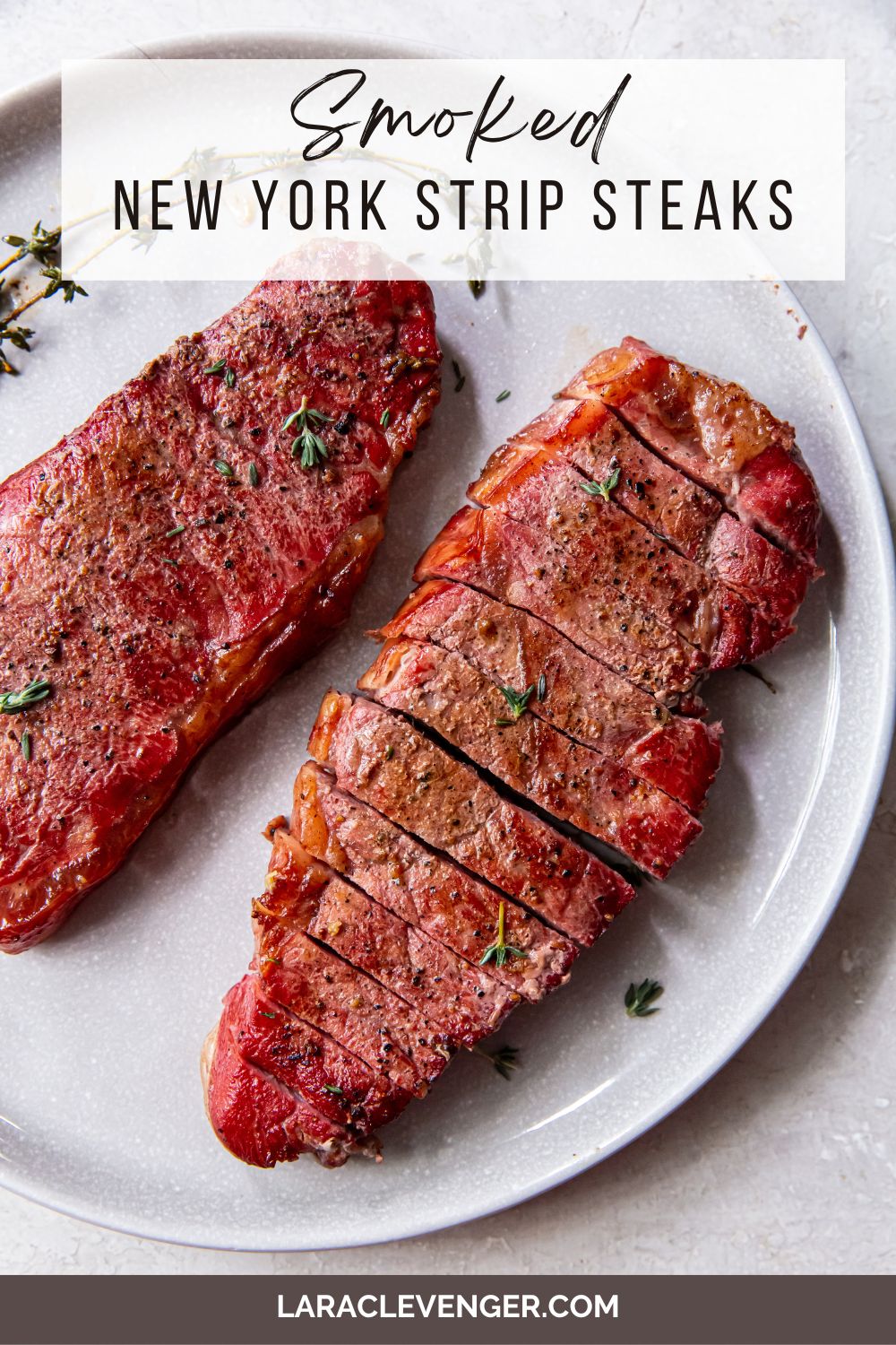 pin of Smoked New York Strip Steaks on a white plate with herbs