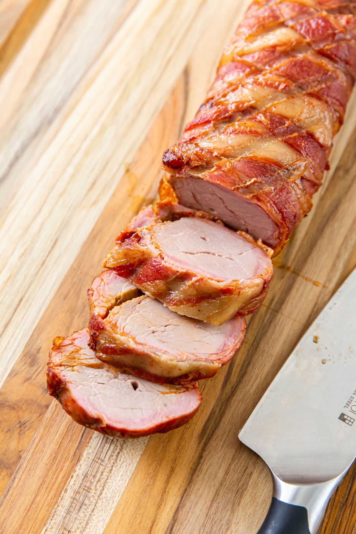 Smoked Bacon Wrapped Pork Tenderloin on a cutting board with a knife