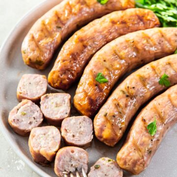 smoked brats on a white plate with a fork and herbs