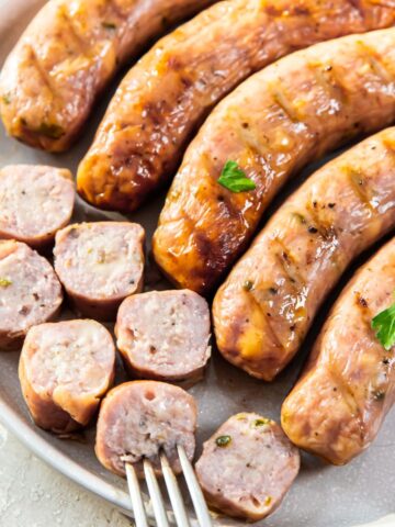 smoked brats on a white plate with a fork and herbs