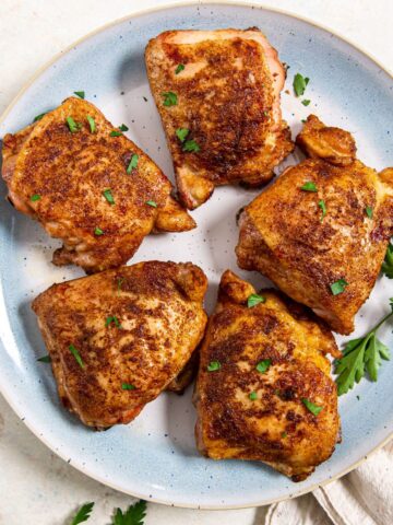 smoked seasoned chicken thighs on a light blue plate with herbs on the side