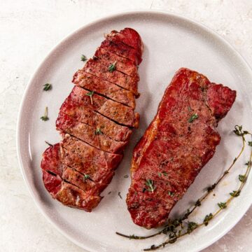 Smoked New York Strip Steaks on a white plate with herbs
