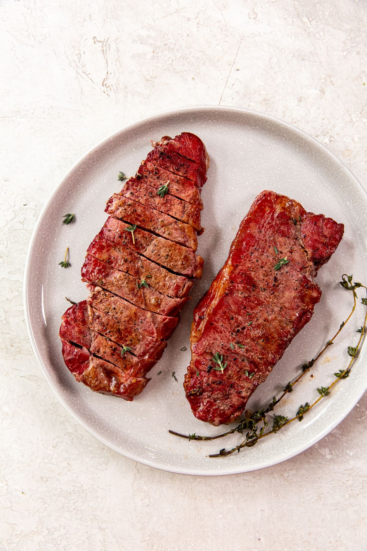 Smoked New York Strip Steaks on a white plate with herbs