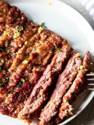 smoked turkey steaks on a white plate with herbs on the side with a fork on the side