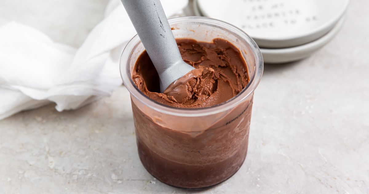 Chocolate Dairy Free Keto Ice Cream in the ninja creami pint with an ice cream scooper in it.