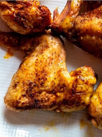 Close-up of seasoned and smoked chicken wings on a white plate, perfectly cooked to tantalizing perfection.