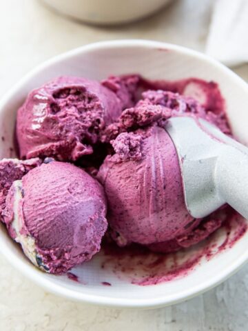 Blueberry ice cream in a bowl with a spoon, topped with purple sprinkles.